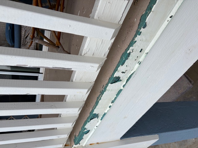 Close-up of an oceanside railing with severe paint peeling, teal undercoat exposed where salt air has eaten through prior topcoats