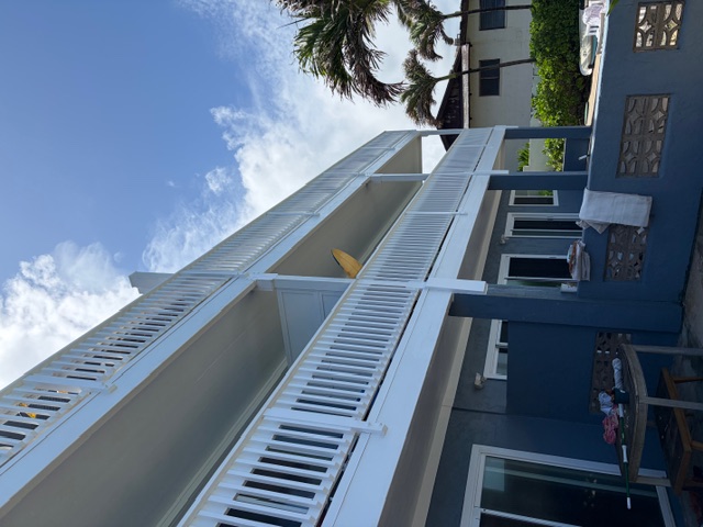 Three-story oceanfront residence with crisp white railings on every floor, freshly finished and sealed against ongoing salt-air exposure, palms visible at the side